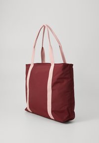 Burgunder farget toteveske med lyserosa, vevde håndtak, rektangulær form, glatt tekstur og minimalistisk design. Ingen synlig maskinvare eller aksenter.