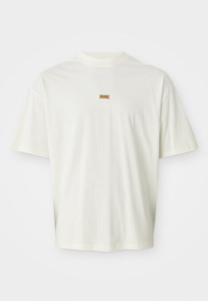 Prosty biały t-shirt z krótkim rękawem z małą prostokątną brązową metką z napisem "HUGO", umieszczoną centralnie pod linią dekoltu.