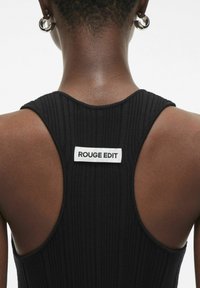 Sort ribbet tanktop med racerback-design og et hvidt mærke med "ROUGE EDIT" på ryggen. Glat tekstur og tætsiddende pasform.