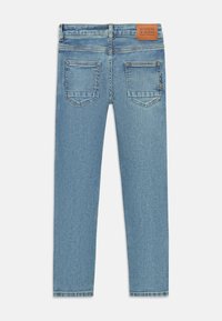 Jean skinny en denim bleu clair. Comprend des poches arrière, un patch logo orange au niveau de la taille, et une texture lisse avec des coutures fines.