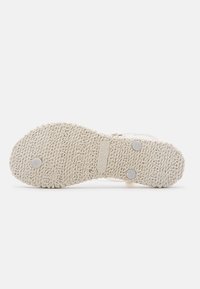 Cream-colored shoe sole with a textured rubber surface, featuring circular metal studs and embossed size and brand information.