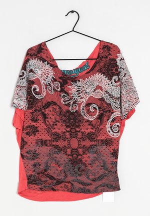 Rood shirt met korte mouwen met witte en zwarte paisley- en bloemmotieven, hangend aan een zwarte hanger tegen een witte achtergrond.