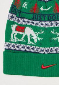 Căciulă tricotată verde cu model de reni alb și roșu, dungi albastre și albe, și logo-ul Nike roșu pe manșetă. Textură moale.