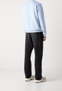 Sweatshirt bleu clair avec des poignets et un ourlet côtelés, associé à un pantalon en denim noir. Les poches arrière visibles et les baskets beige complètent la tenue.