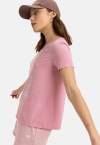 Camiseta de algodón rosa con mangas cortas y cuello redondo, que presenta un diseño gráfico blanco. Combinada con pantalones cortos rosa a juego.