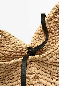 Torebka z plecionej słomy z teksturowanym, naturalnym wykończeniem, z czarnym skórzanym paskiem i węzełkiem na górze do mocowania.