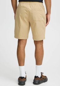 Khaki shorts with a stretchy waistband, back pocket, and smooth fabric. Worn with black and brown sneakers and white crew socks.