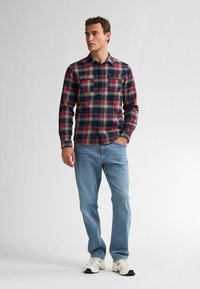 Geklede flanellen overhemd in marineblauw, rood en wit; twee borstzakken; gecombineerd met lichtblauwe jeans en witte sneakers. Casual fit.