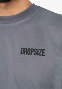 Grå bomulds T-shirt med rund halsudskæring og korte ærmer, prydet med et iøjnefaldende "DROPSIZE" logo i sort på forsiden.