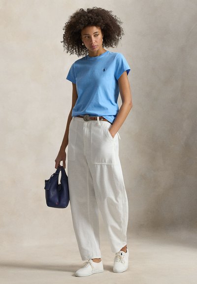 Ανοιχτό μπλε βαμβακερό T-shirt με κοντά μανίκια, λευκό παντελόνι σε χαλαρή εφαρμογή, λευκά αθλητικά παπούτσια και σκούρα μπλε τσάντα ώμου. Ζώνη με υφή και στρογγυλή αγκράφα.