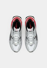 Αθλητικά παπούτσια σε ασημί και λευκό, με επάνω μέρος από δίχτυ, μαύρες λεπτομέρειες, κόκκινες επισημάνσεις και υφασμένα επιφάνειες με εμφανές λογότυπο.