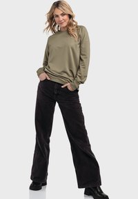 Olivenfarbene Sweatshirt mit langen Ärmeln und gerippten Bündchen, kombiniert mit schwarzen weiten Jeans. Das Outfit zeichnet sich durch eine lockere Passform und eine weiche Textur aus.