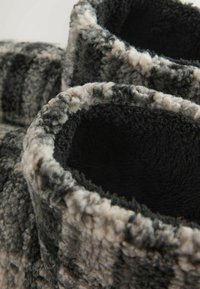 Textúrované, útulné papuče s čiernym interiérom a vonkajšou vrstvou mäkkej, chlpatej šedej a krémovej vzorovanej látky. Okrúhly, otvorený dizajn.