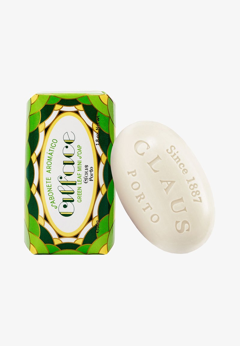 Eine grüne box mit Blättermuster enthält eine weiße ovale Seife mit erhabenem Text. Das Etikett der Seife lautet "Claus Porto, Seit 1887."