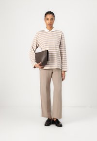 Striped long-sleeve polo in cream, beige, and pink. Paired with beige straight-leg trousers and a dark brown clutch. Black shoes complete the look.