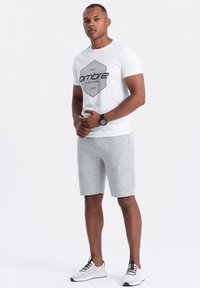 T-shirt blanche avec impression graphique noire et design en hexagone, associée à un short gris clair et des baskets blanches avec des accents noirs.
