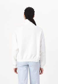 Vit tröja med hög krage och ribbad nederkant. I kombination med ljusblå och vita randiga byxor. Slät textur.