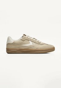 Beige sneaker med en glat læderoverdel med anklædninger af ruskind, gummisål, rund tå og tonale syninger. Klassisk snørebåndsdesign.