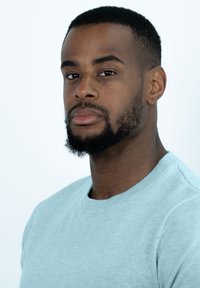 Lichtblauwe gebreide trui met een ronde hals, met een gladde textuur en ribbelaccenten bij de halslijn. Close-upportret van een man.