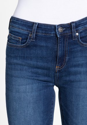 Jeans de mezclilla en azul oscuro con una textura suave, con cremallera, cierre de botón y dos bolsillos frontales. Detalle de costura en contraste visible.