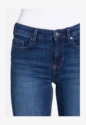 Džínové kalhoty v tmavě modré barvě s hladkým povrchem, s zipem na přední straně, knoflíkovým zapínáním a dvěma předními kapsami. Viditelný kontrastní steh.