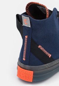 Námořnické plátěné vysoké tenisky s černými akcenty, oranžovým prošíváním a gumovou podrážkou, na které se nachází oranžové logo "CONVERSE ALL STAR" na patě.