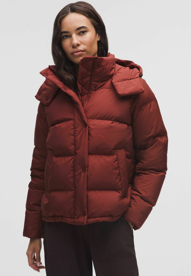 Rød puff jakke med høj krave, quiltet design og knaplukninger. Har hætte og sidelommer. Glat, skinnende tekstur.