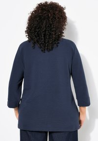 Marineblaues Langarmoberteil aus strukturiertem Stoff, lockerer Schnitt und mit Manschettenärmeln. Es hat einen runden Halsausschnitt und keine sichtbaren Muster oder Akzente.