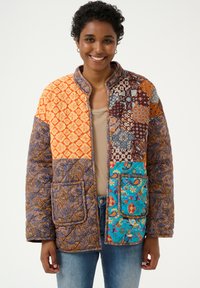 Jachetă matlasată cu design patchwork, având culorile portocalie, albastră, maro și diverse modele intricate. Include buzunare și un guler înalt.