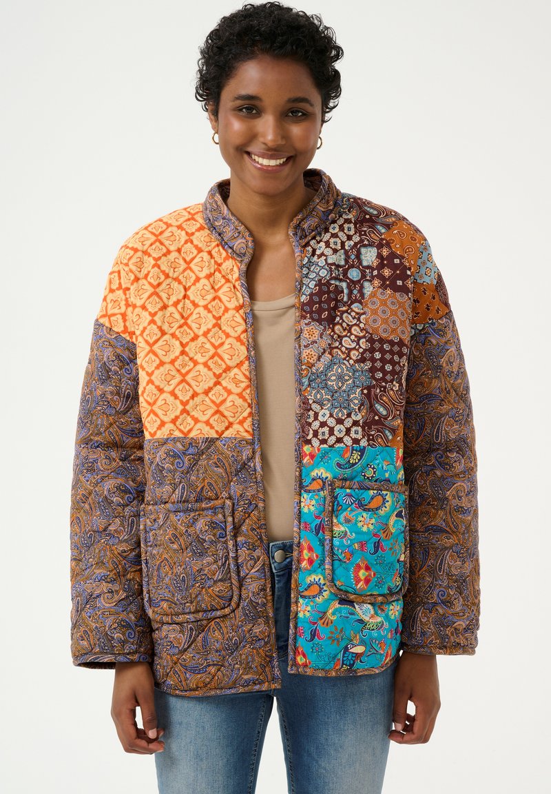 Jachetă matlasată cu design patchwork, având culorile portocalie, albastră, maro și diverse modele intricate. Include buzunare și un guler înalt.