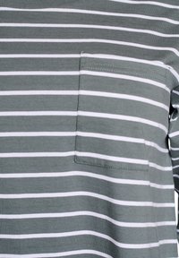 T-shirt a righe in cotone grigio-verde con strisce orizzontali bianche. Presenta una tasca sul petto e una texture morbida. Design semplice con colletto girocollo.