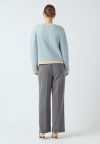 Jasnoniebieski sweter o fakturze z beżowymi wykończeniami, zestawiony z szarymi, szerokimi spodniami. Buty to beżowe szpilki, prezentujące prosty i nowoczesny styl.