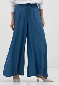 Pantaloni in denim a gamba larga di colore blu scuro, con cintura elastica. Il tessuto appare liscio e ha una consistenza morbida.