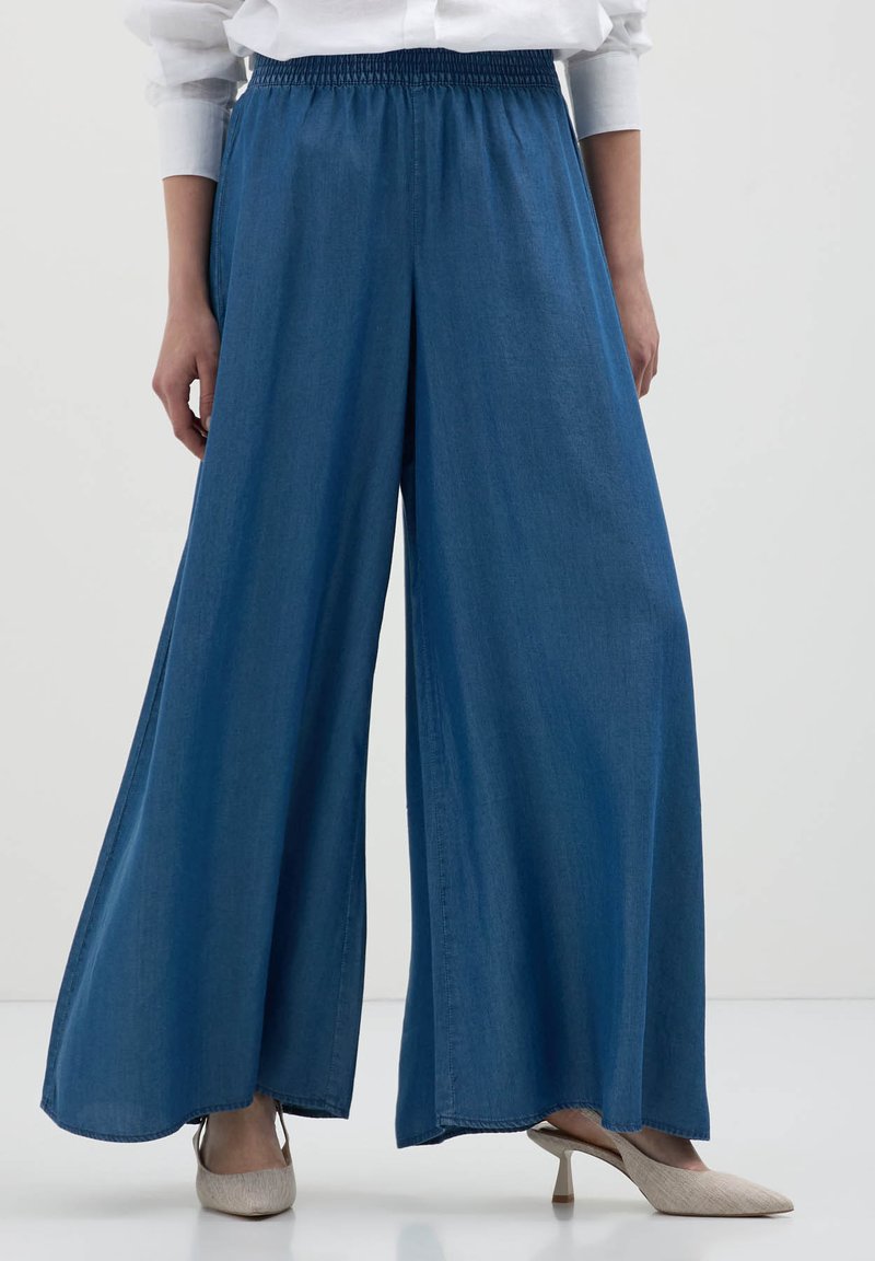 Pantaloni in denim a gamba larga di colore blu scuro, con cintura elastica. Il tessuto appare liscio e ha una consistenza morbida.