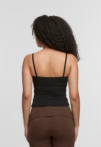 Black fitted camisole with thin straps, ribbed texture, and a scoop back design. Worn with brown high-waisted leggings.