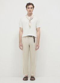 Camicia bianca a maniche corte, pantaloni beige rilassati con finitura testurizzata, sandali intrecciati marroni e una sciarpa di seta stampata attorno al collo.