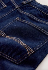 Mørkeblåt denimstof med detaljerede orange syninger, der afgrænser en baglomme på et par jeans.