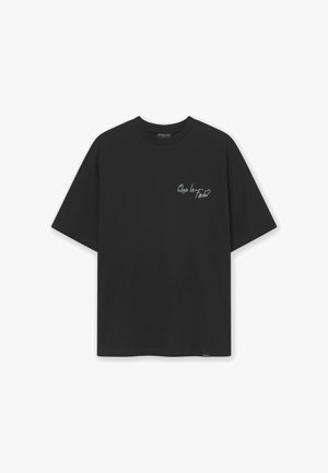 Black cotton t-shirt with short sleeves and a crew neck. Features blue text on the left chest area reading "Que le pasa?"