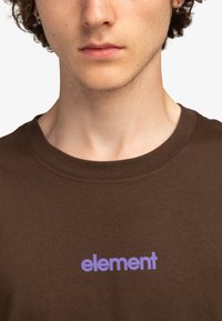 Camiseta de algodón marrón con un logo "element" en púrpura. Cuello redondo y mangas cortas, con una textura suave y un diseño minimalista.