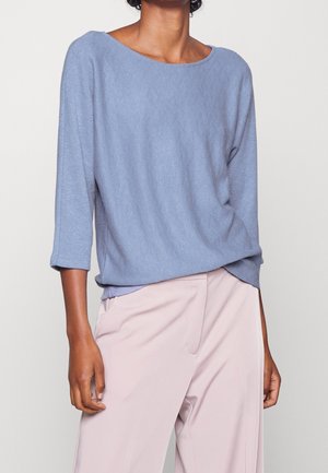 Maglione in maglia tessuta azzurro chiaro, con scollo ampio e maniche a tre quarti, abbinato a pantaloni rosa chiaro.