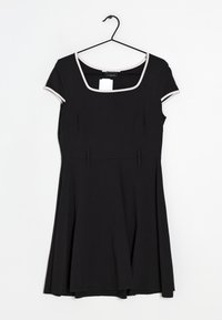 Černé šaty s krátkými rukávy, čtvercovým výstřihem a kontrastním bílým lemováním kolem výstřihu a okrajů rukávů. Obsahují dva přední smyčky.