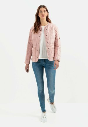 Lys pink quiltet jakke med trykknapper, der har to forlommer. Båret over en hvid skjorte og parret med blå jeans og hvide sneakers.