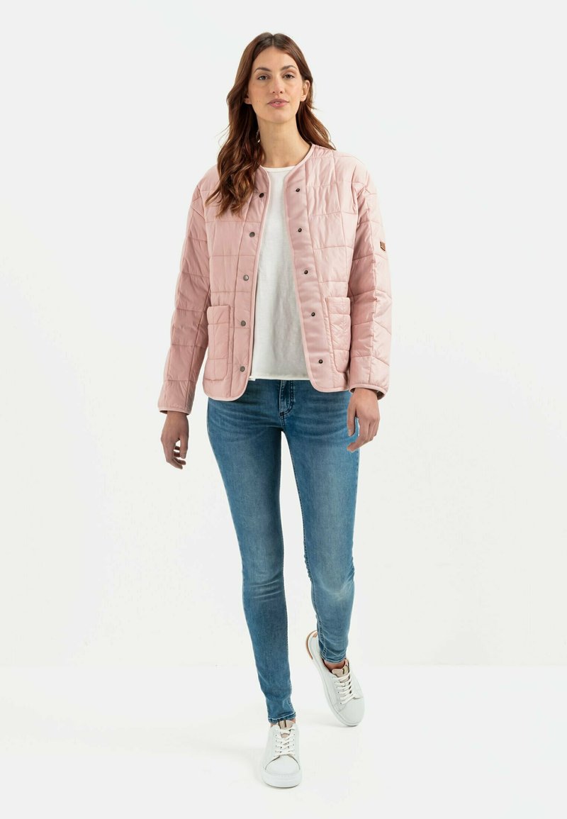 Lys pink quiltet jakke med trykknapper, der har to forlommer. Båret over en hvid skjorte og parret med blå jeans og hvide sneakers.