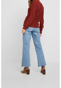 Pull en tricot bordeaux, jeans bleu évasés et chaussures à talons marron avec un imprime serpent. Tenue décontractée avec un matériau texturé et un ourlet effiloché.