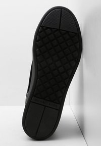 Černá podešev tenisky s texturovaným diamantovým vzorem a hladkými částmi, se značkováním a silnou, odolnou gumovou konstrukcí.