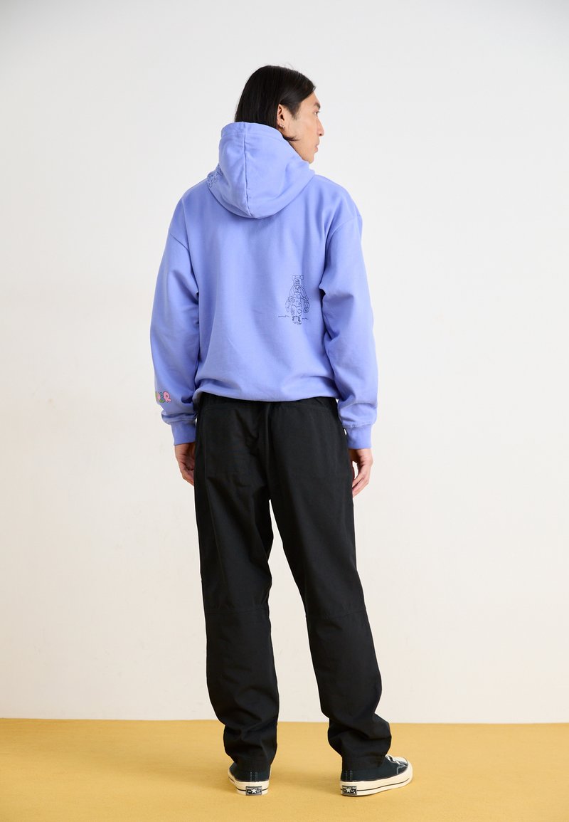 Purple hooded sweatshirt with a graphic design on the back, paired with black trousers and dark shoes. Simple, casual outfit.