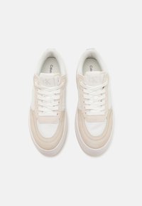 Hvite og lys beige joggesko med snøring, i semsket og glatt stoff, avrundet tå og teksturert gummisåle. Logo på tungen.