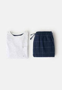 Tricou gri din bumbac cu un buzunar pe piept, asociat cu pantaloni scurți în carouri bleu marin, cu talie elastică și șnur.