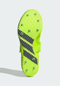 Bright yellow athletic shoe sole featuring a textured grip pattern, black accents, and removable studs for traction on various surfaces.