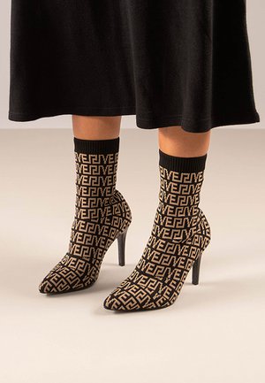 Botines de calcetín en negro y beige con un alto tacón de aguja, que presentan un patrón geométrico en toda la tela y un puño de tobillo acanalado.